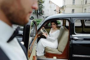 Beautiful happy young bride and groom looking from retro auto