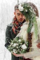 Beautiful bride and groom with a white dog are standing on the background of a snowy forest. photo