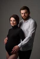 una mujer embarazada y su esposo se abrazan en un fondo gris. pareja esperando un bebé. foto