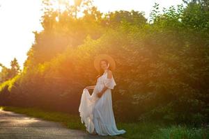 Pregnant woman in a hat posing in a dress on a background of green trees. photo