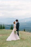 La novia y el novio jóvenes y elegantes se paran en un bote en el fondo del cielo nublado, el mar y las montañas de montenegro. foto