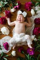 una niña de dos meses yace sobre una mesa con peonías. foto