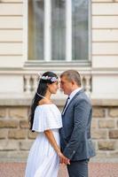 Wedding photo session on the background of the old building. The groom watches his bride posing. Rustic or boho wedding photography.
