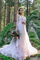 novia feliz con un vestido de novia rosa. la chica tiene un ramo de novia en sus manos. ceremonia de boda estilo boho en el bosque. foto