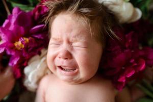 A little two-month-old girl lies on a table with peonies. photo