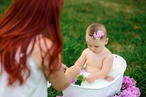 mamá ayuda a su pequeña hija de un año a bañarse en el baño. filmado en un parque al aire libre en la naturaleza. foto