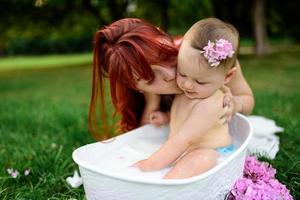 Mom helps her little one-year-old daughter bathe in the bathroom. Filmed in a park outdoors in nature. photo