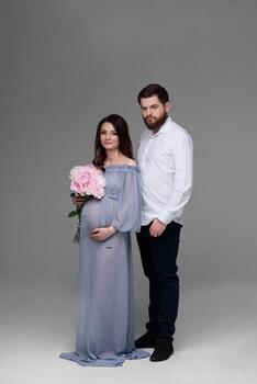 A pregnant woman and her husband are hugging on a gray background in the studio. photo