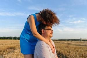 Adult farmer and wife spend time in the field. The man is sitting. A woman stands next to him and hugs him. A woman kisses her husband on the head. photo