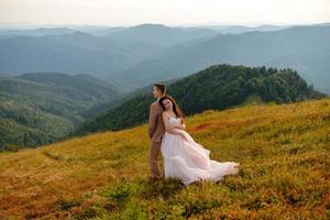 La novia y el novio jóvenes y elegantes se paran en un bote en el fondo del cielo nublado, el mar y las montañas de montenegro.