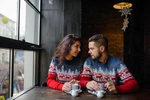 pareja feliz y romántica en suéteres cálidos beben café de vasos de papel desechables en la cafetería. vacaciones, navidad, invierno, amor, bebidas calientes, concepto de personas foto