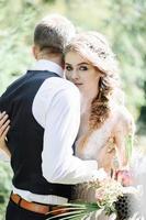 atractiva pareja de recién casados, momento feliz y alegre. el hombre y la mujer con ropa festiva se sientan en las piedras cerca de la decoración de la boda al estilo boho. ceremonia al aire libre. foto