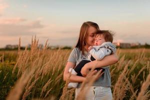 A mother walks in the field with her little daughter in her arms. photo