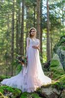 Happy bride in a pink wedding dress. The girl holds a wedding bouquet in her hands. Boho style wedding ceremony in the forest. photo