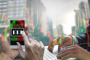 Double exposure of businessman Hand use smartphone and laptop trading online on screen with Candle stick graph chart of stock market and city background
