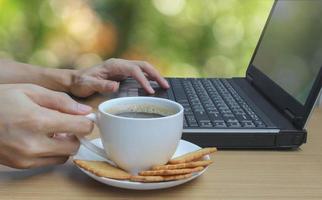 Hands drinking coffee and using laptop and bokeh background photo