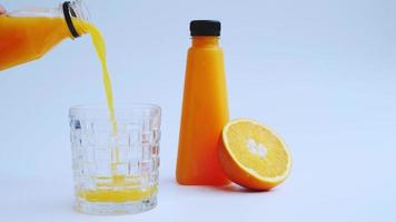 despeje o suco de laranja em uma jarra de vidro em um fundo branco e tenha a garrafa de suco de laranja pronta. laranja cortada ao meio como plano de fundo video