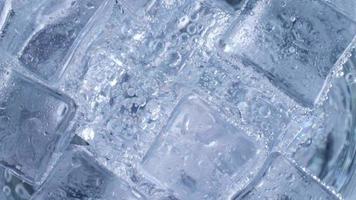 los cubitos de hielo con burbujas de aire se arremolinan en el vaso. agua de soda y enfriar en un vaso transparente. video