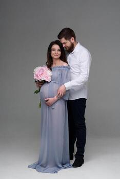A pregnant woman and her husband are hugging on a gray background in the studio. photo