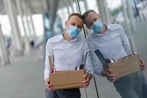 The fired office worker fell to his knees and covered his face due to stress. In front of him is a cardboard box with stationery. The man is unhappy due to a reduction in the robot. photo