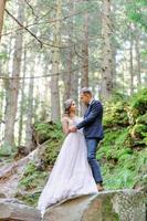 una atractiva pareja de recién casados, un momento feliz y alegre. un hombre y una mujer se afeitan y se besan con ropa de fiesta. ceremonia de boda de estilo bohemio en el bosque al aire libre. foto