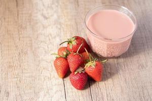 Strawberry flavored milk in clear glass on wooden background photo