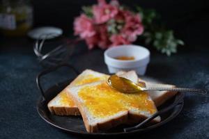 pan untado con mermelada de naranja en una bandeja vintage en tonos negros. foto