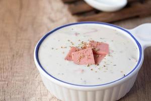 Cheese soup with vegetables and ham with toast on the table close-up horizontal sprinkle oregano in white bowl