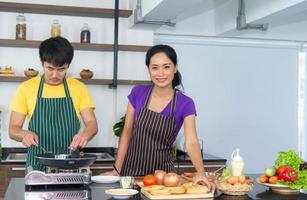 Una pareja asiática romántica y encantadora disfruta y cocina feliz en la cocina foto