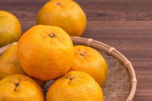 Fresh, beautiful orange color tangerine on bamboo sieve over dark wooden table. Seasonal, traditional fruit of Chinese lunar new year, close up. photo