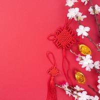 concepto de diseño del año nuevo lunar chino - hermoso nudo chino con flor de ciruelo aislado sobre fondo rojo, plano, vista superior, diseño superior. foto