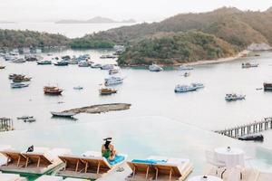 vista trasera de una mujer sentada en una silla relajante disfrutando de la vista del mar con muchos barcos desde arriba foto