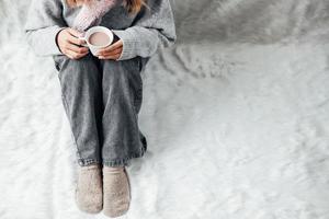 A girl with winter clothes enjoying a cup of hot drink on winter season at home photo