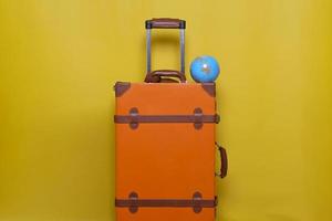 maleta naranja con miniglobo aislado en fondo amarillo para concepto de viaje con estilo mínimo foto