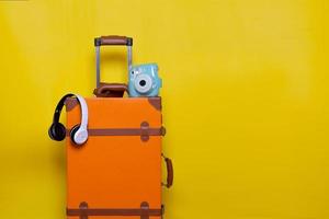 maleta naranja con auriculares inalámbricos y mini cámara aislada en fondo amarillo para el concepto de viaje con un estilo minimalista foto