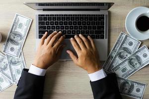 hombre de negocios que trabaja con una computadora portátil con billetes de dólar en el escritorio de la oficina