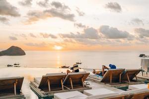 una pareja tumbada en una silla relajante disfrutando de la puesta de sol con vistas al mar foto