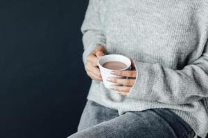 manos de mujer con ropa de invierno de manga larga sosteniendo una taza de chocolate caliente foto