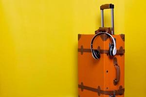 maleta vintage naranja con auriculares inalámbricos aislados en fondo amarillo para concepto de viaje con estilo minimalista
