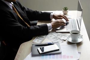 Businessman working with laptop with dollar bills around at office desk photo