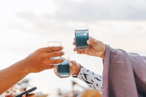 manos de la gente animando con un vaso de cóctel azul tropical foto
