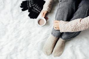 Top view of woman in winter clothes and socks holding a hot chocolate drink