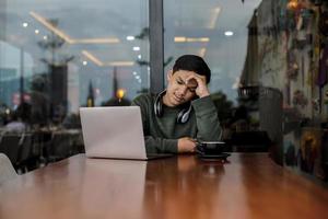 estudiante universitario asiático confundido mientras estudiaba usando una computadora portátil en la cafetería o cafetería foto