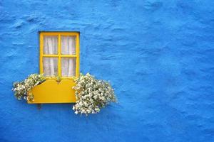 rustic blue cottage wall with yellow window frame and flower box photo