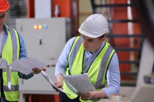 ingeniero industrial masculino con casco de seguridad mientras está de pie en una fábrica industrial pesada. el mantenimiento que busca trabajar en maquinaria industrial y verificar la configuración del sistema de seguridad en fábrica. foto