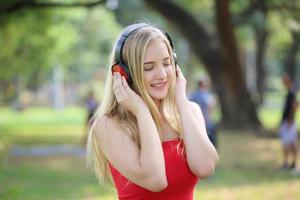 hermosa mujer rubia de pie mientras escucha música en los auriculares en el parque. foto