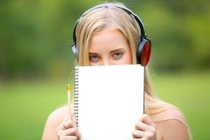 Beautiful blonde woman standing by holding note cover half of her face and wearing headphone. photo