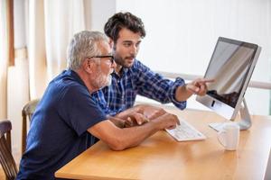 adult man teaching elderly man to using computer at home. photo