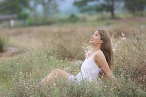 hermosa mujer joven sentada en el campo de hierba verde y soplando diente de león. al aire libre. disfruta de la naturaleza. niña sonriente saludable en el césped de primavera. concepto libre de alergias. libertad foto