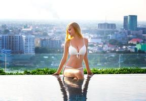 mujer joven disfrutando de un sol, modelo de niña delgada en bikini blanco junto a la piscina.
